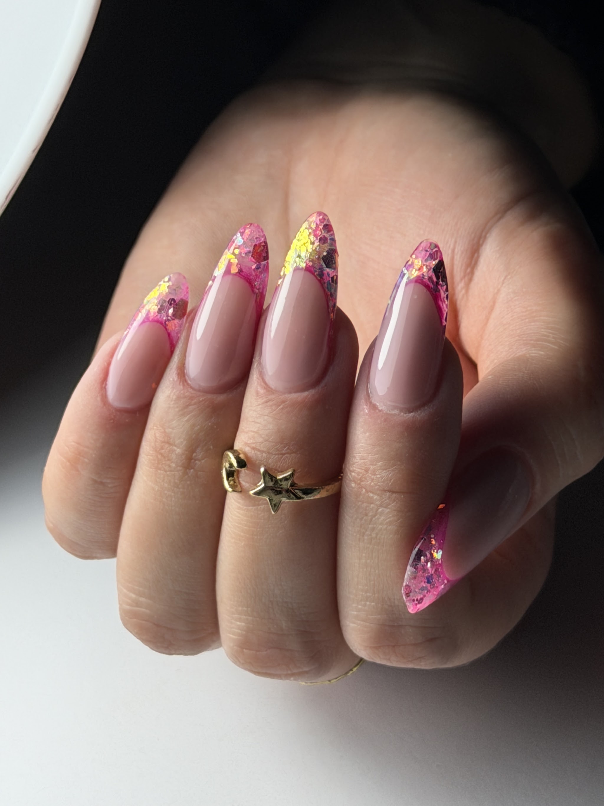Amandelvormige nagels in nude met roze glitter op de toppen en een gouden ring