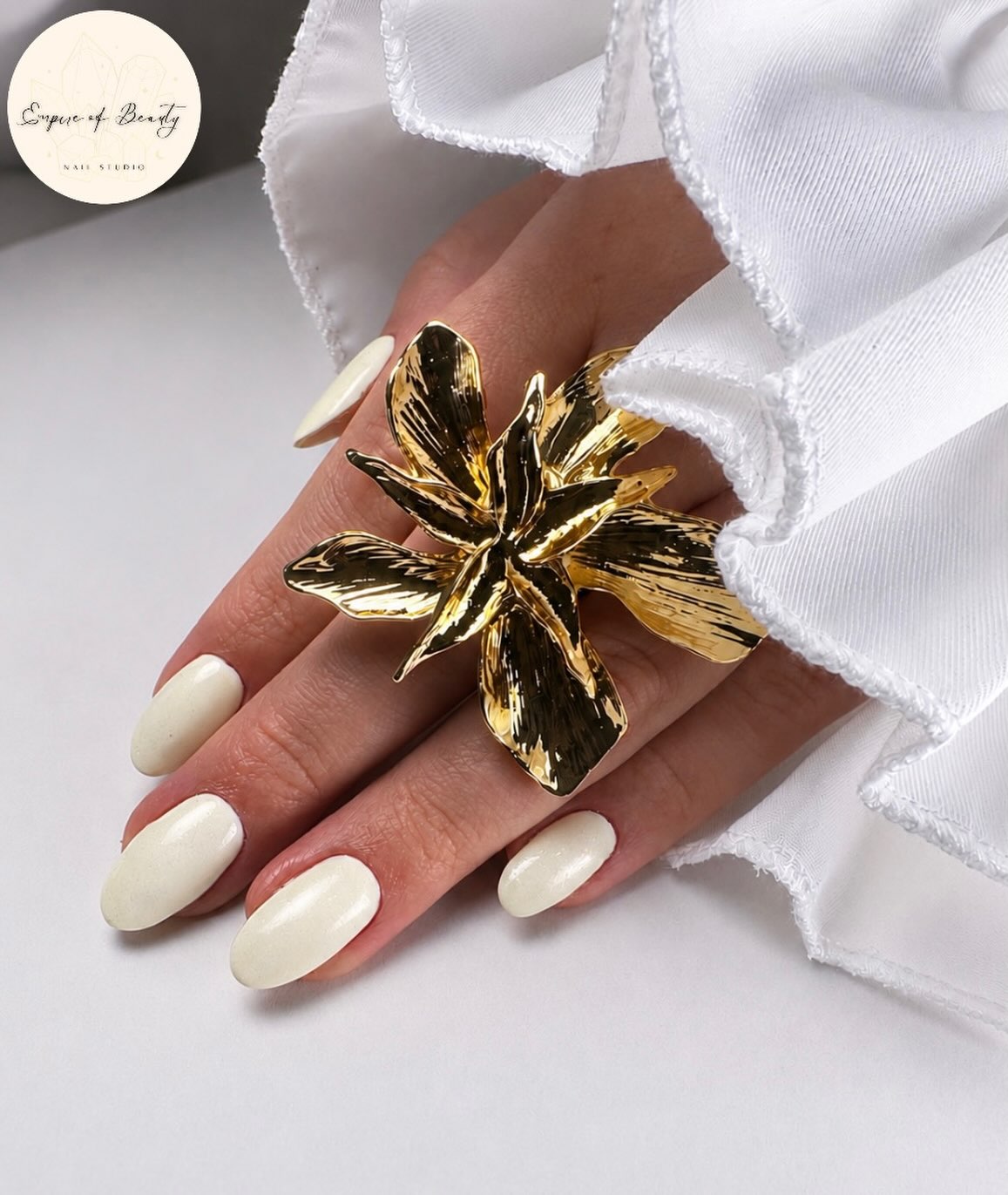 Melkwitte gelnagels met een grote gouden bloemring